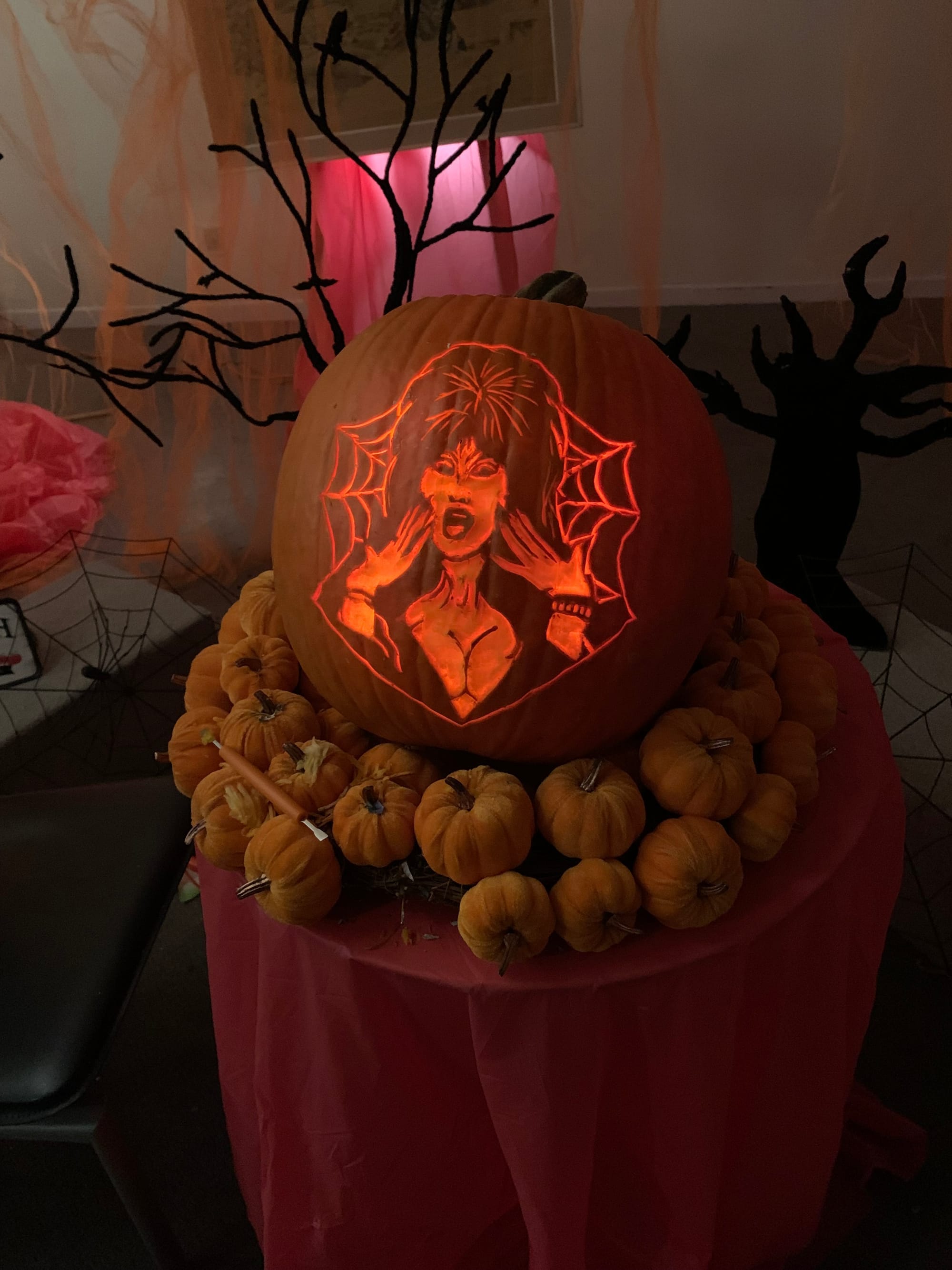 Illuminated pumpkin carved with a long-haired figure, displayed with autumn decorations.