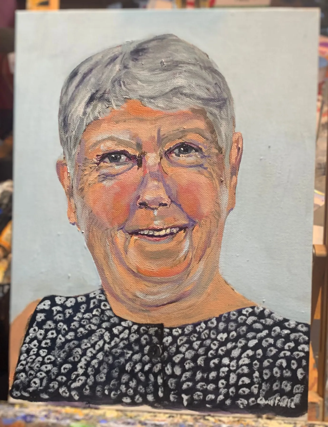 Portrait painting of a smiling woman with short grey hair and a dark patterned blouse.