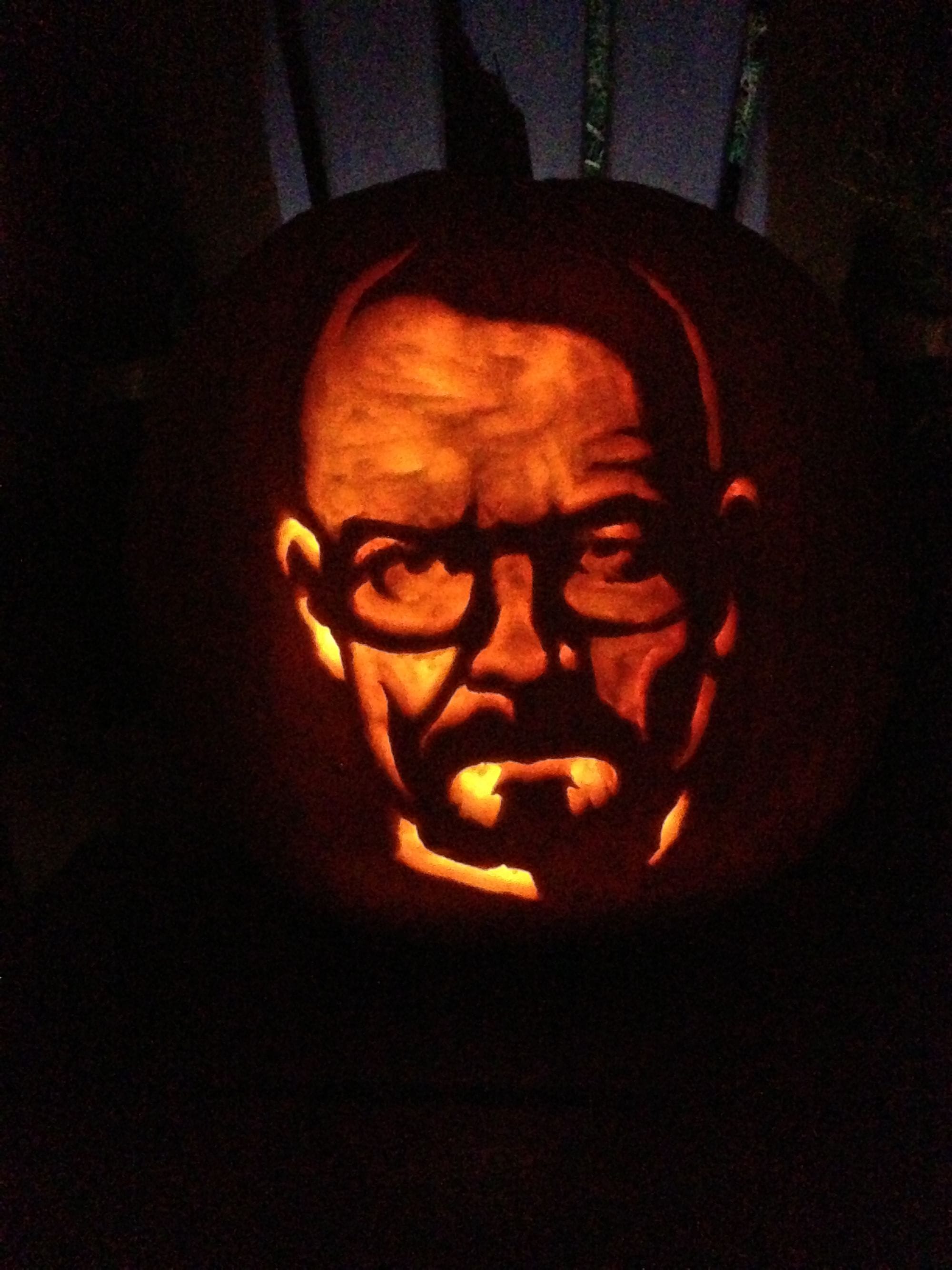 Illuminated pumpkin carved with a stern face wearing rectangular glasses.
