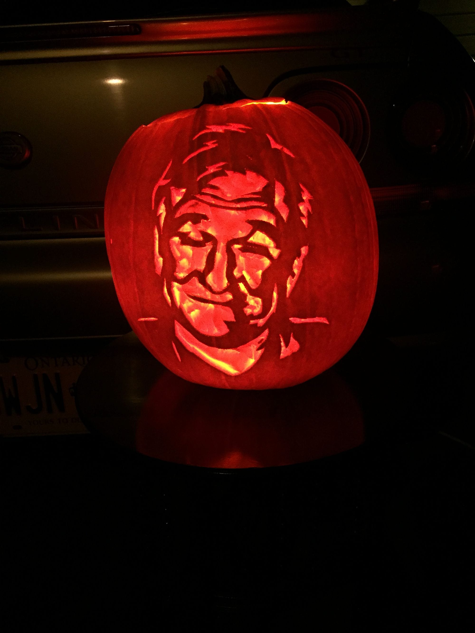 Illuminated pumpkin carved with a smiling, short-haired face.