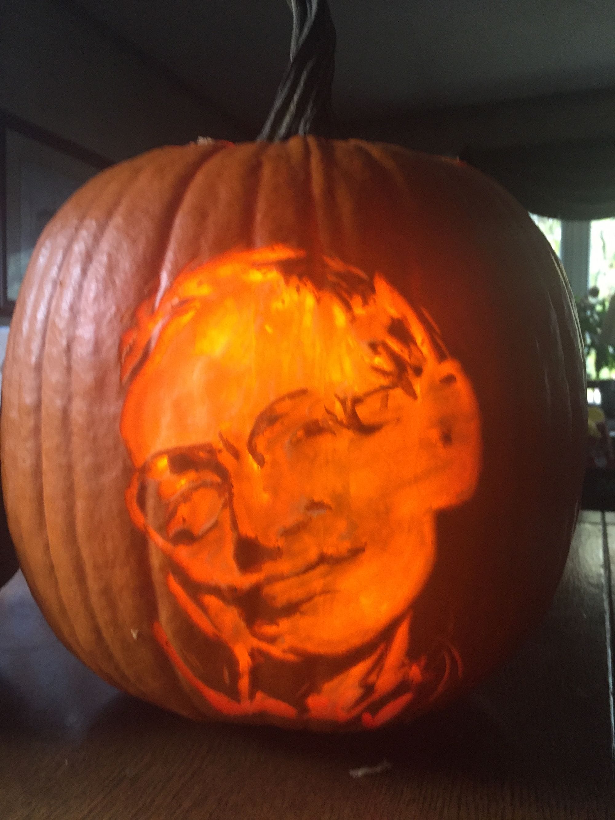 Pumpkin carving of a face with round glasses, illuminated from within.
