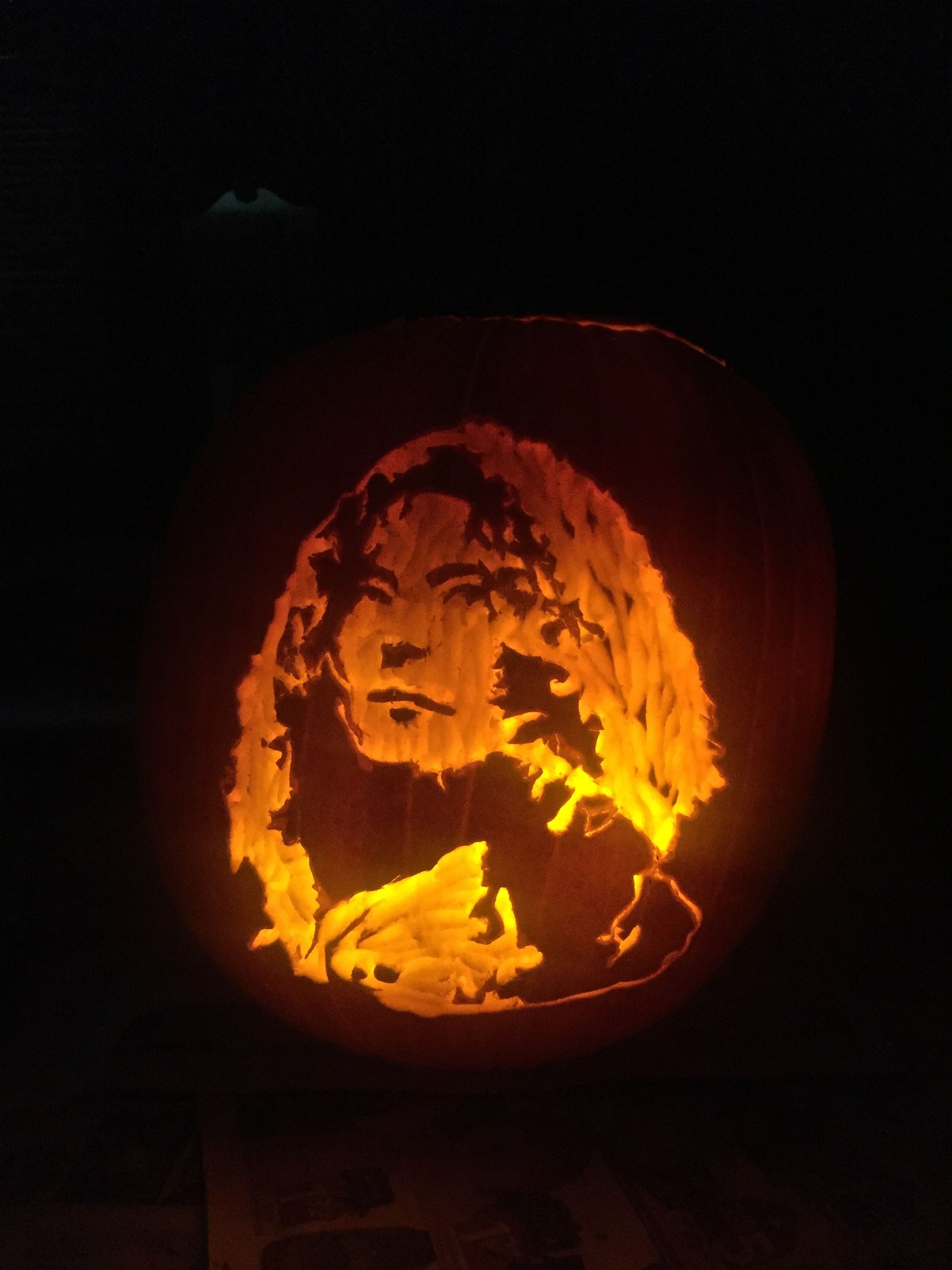Illuminated pumpkin carved with a curly-haired face.