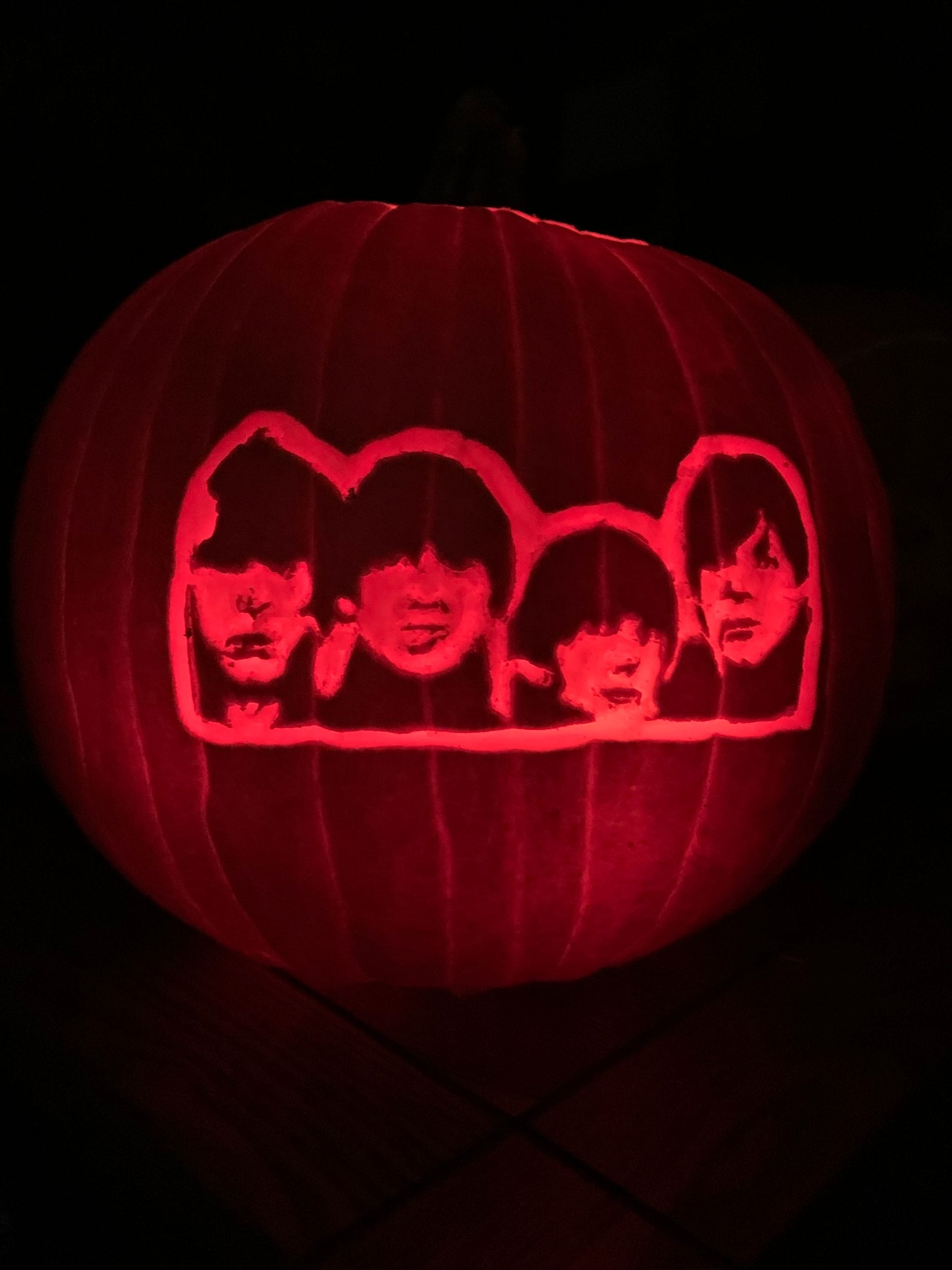 Illuminated pumpkin carved with a row of four stylized faces.