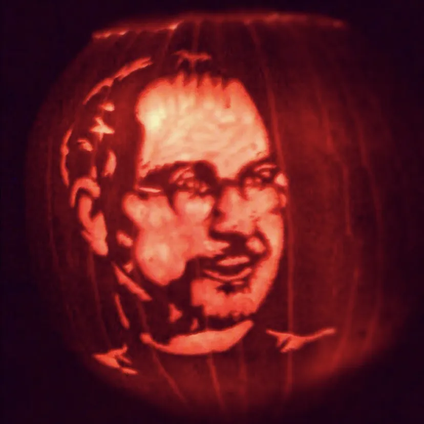 Illuminated pumpkin carved with a bespectacled face and short beard.