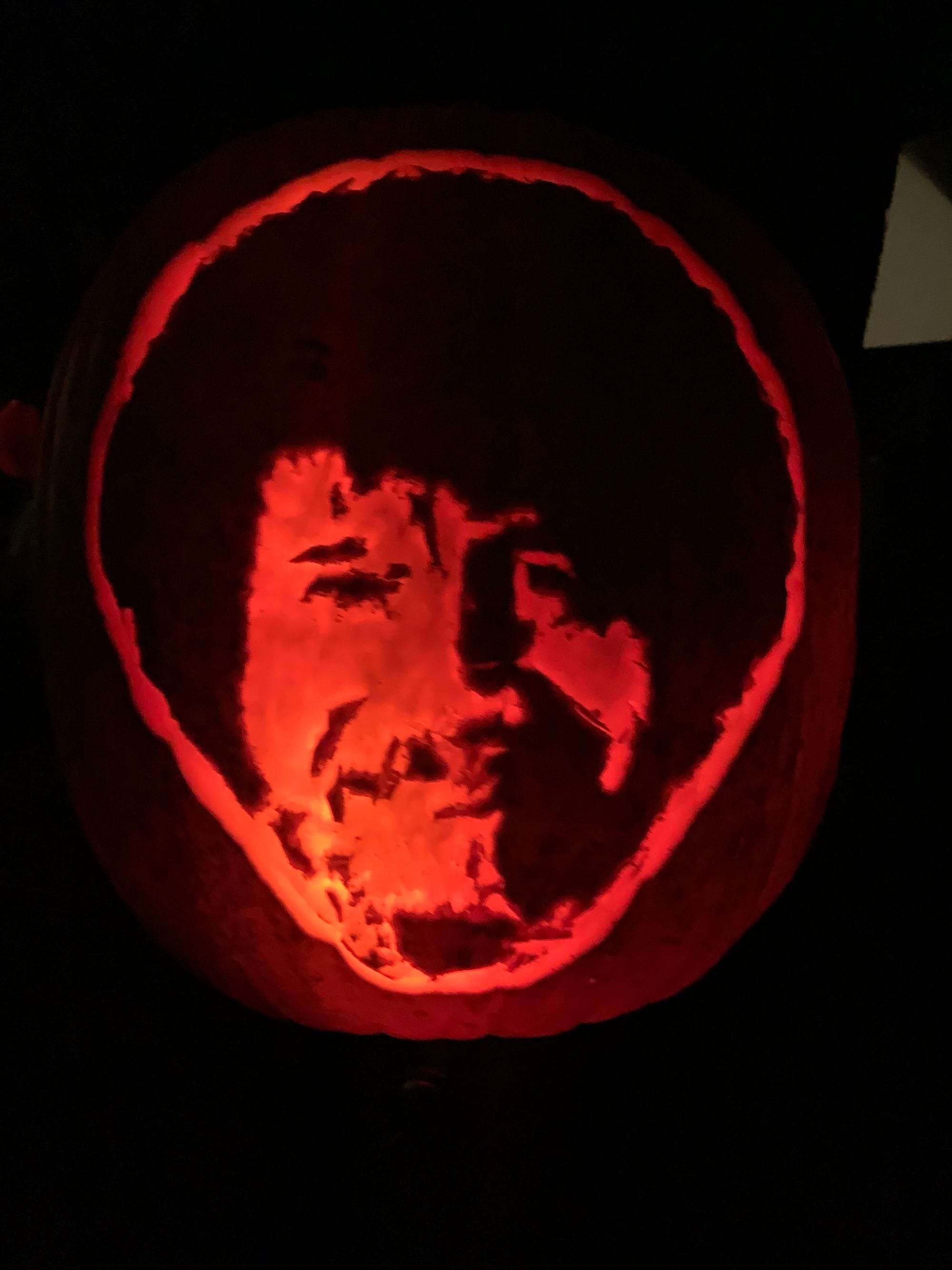 Illuminated pumpkin carved with a smiling face and rounded curly hair.