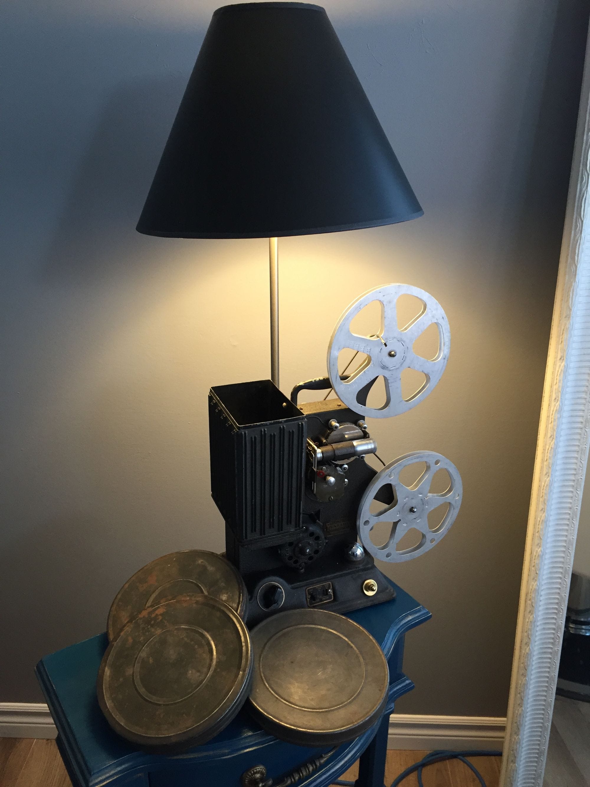 Table lamp assembled from a film projector and film reels beneath a dark shade.