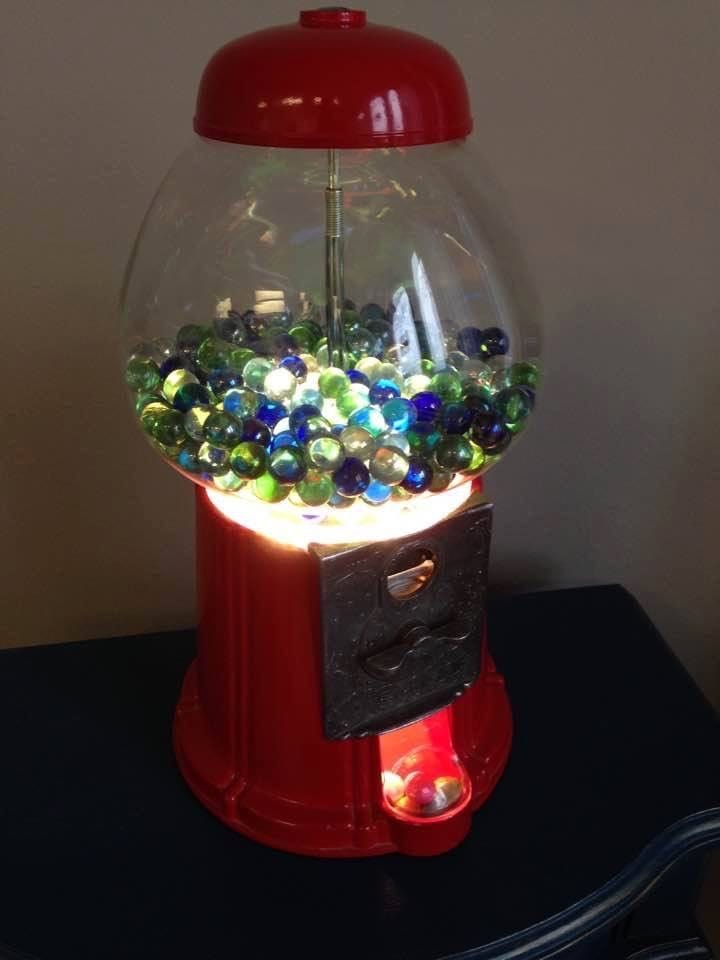 Red gumball-machine form filled with illuminated coloured glass marbles.