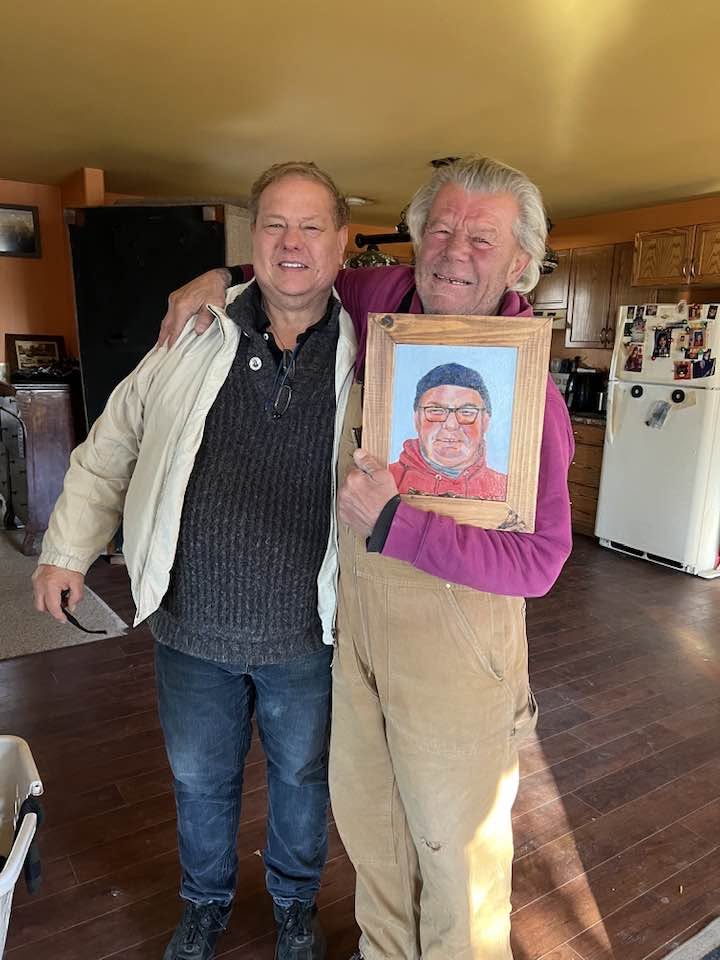 Two men standing together with the framed portrait of Ernie.