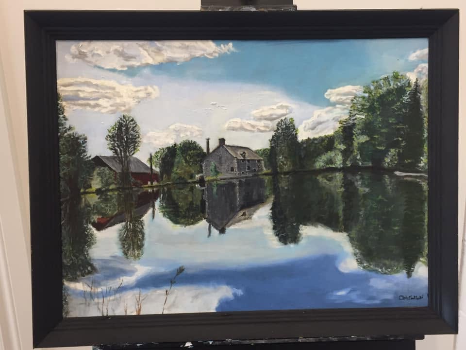 Framed landscape painting of waterside buildings and trees reflected in still water at Upper Canada Village.